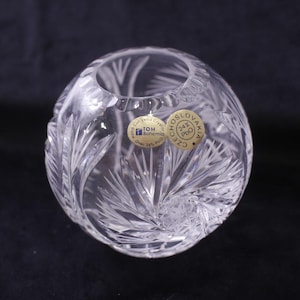 以下が含まれることがあります： 透明で丸いクリスタル花瓶。葉と羽の模様が彫られています。花瓶には広い開口部があり、「CZECHOSLOVAKIA」と「TOM Bohemia」と書かれたステッカーが付いています。クリスタルは光を反射し、きらめく効果を生み出します。