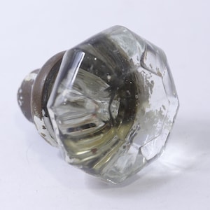 May include: A clear, faceted glass doorknob with a tarnished metal base. The knob has a geometric design and is likely vintage. The metal base shows signs of wear, with chipped paint. The doorknob is a decorative hardware item.