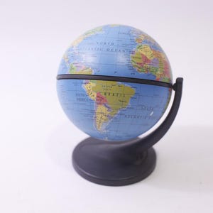 May include: A blue and black globe with a detailed world map. The globe is mounted on a black stand with a curved support. The continents are depicted in various colors, and the oceans are blue.