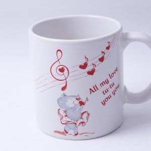 May include: White ceramic mug with a red musical note design and a cartoon illustration of a gray cat singing. The text on the mug reads "All my love tu-tu you you".