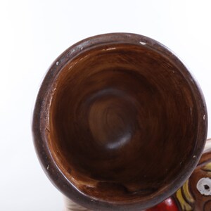 Op de afbeelding: Een bruin keramieken clownbeeldje met een grote, open mond trompet. De clown heeft een geschilderd gezicht met een rode neus, witte tanden en kleurrijk haar. De trompet is donkerbruin van kleur.