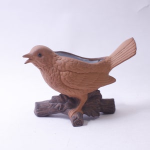 May include: A brown ceramic bird planter with a textured surface. The bird is perched on a branch with a small pot for planting.