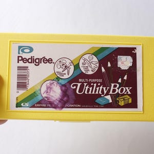 May include: A bright yellow rectangular plastic utility box featuring a label with the text Pedigree Multi-Purpose Utility Box, Empire Plastic Corporation, and illustrations of small hardware, fishing lures, pencils, an eraser, and a sharpener.