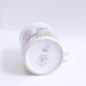 May include: White ceramic Care Bears mug with a colorful illustration of the Care Bears. The mug has a handle and the text "Stoneware Designers Collection" on the bottom.