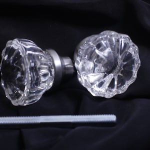 May include: Two clear glass door knobs with a silver metal base. The knobs have a faceted design and are shown on a black fabric background.