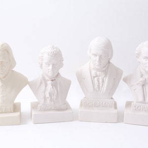 May include: Four white plaster busts of famous composers on individual bases. The busts are of Liszt, Mozart, Schumann, and Schubert. Each base has the composer's name printed on it.