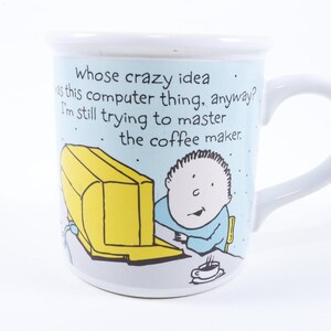 May include: White ceramic mug with a humorous cartoon design. The mug features a yellow computer, a person, and the text: "Whose crazy idea was this computer thing, anyway? I'm still trying to master the coffee maker."