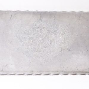 May include: A silver serving tray with an embossed floral design. The tray has a scalloped edge and is made of aluminum.