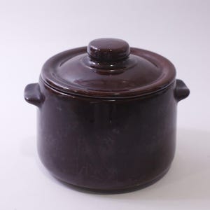Peut inclure: Une marmite en céramique brun foncé avec un couvercle et deux poignées latérales. Le pot a une finition brillante et une forme arrondie. Le couvercle a un petit bouton sur le dessus. Cet article de cuisine est adapté à la cuisson et au service.