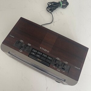 Pu&ograve; includere: Un radio sveglia stereo in legno marrone con un quadrante argentato e pulsanti neri. La radio ha un display digitale dell'orologio, un timer di spegnimento e un pulsante snooze. La radio ha anche un selettore di canali, una manopola del volume e un pulsante di accensione.