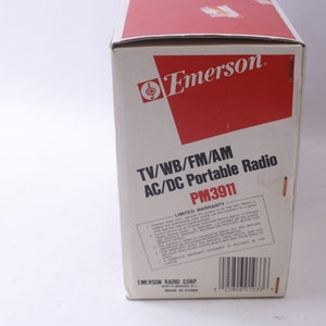 May include: A vintage Emerson portable radio box. The box is white with red accents and features the Emerson logo. Text on the box reads "TV/WB/FM/AM AC/DC Portable Radio PM3911" and includes a limited warranty statement.