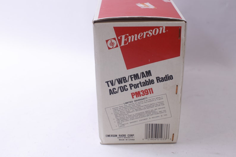 May include: A vintage Emerson portable radio box. The box is white with red accents and features the Emerson logo. Text on the box reads "TV/WB/FM/AM AC/DC Portable Radio PM3911" and includes a limited warranty statement.