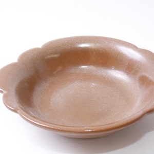 Pode incluir: Uma tigela de cerâmica marrom com uma borda festonada. A tigela está vazia e tem um esmalte salpicado.