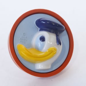 May include: A round, orange plastic knob with a blue and white Donald Duck face. The knob has the text "Walt Disney Prod" on the back.