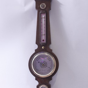 Puede incluir: Estación meteorológica de madera oscura con termómetro, barómetro e higrómetro. El termómetro tiene un líquido rosa y está marcado en grados Celsius. El barómetro tiene una esfera plateada con una aguja.