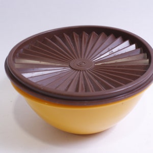 May include: A yellow plastic bowl with a brown plastic lid. The lid has a radial design with a raised center.