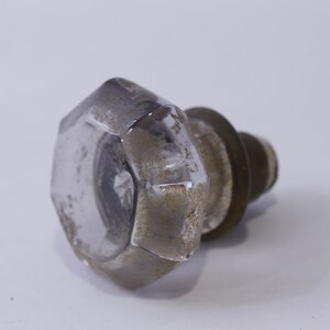 May include: A clear glass door knob with a hexagonal shape and a brass base. The knob has a worn, aged appearance.