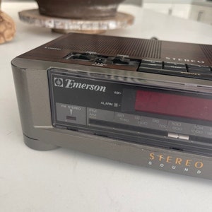Pu&ograve; includere: Una radio stereo AM/FM vintage Emerson con orologio digitale e sveglia. La radio &egrave; grigia e nera con una finitura in legno. La radio ha un display digitale e una variet&agrave; di pulsanti per la sintonizzazione, il volume e altre funzioni. La radio ha anche un timer di spegnimento e un pulsante snooze.
