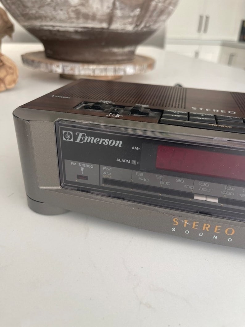 Pu&ograve; includere: Una radio stereo AM/FM vintage Emerson con orologio digitale e sveglia. La radio &egrave; grigia e nera con una finitura in legno. La radio ha un display digitale e una variet&agrave; di pulsanti per la sintonizzazione, il volume e altre funzioni. La radio ha anche un timer di spegnimento e un pulsante snooze.