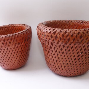May include: Two brown woven baskets of different sizes. The larger basket is wider and taller than the smaller basket.