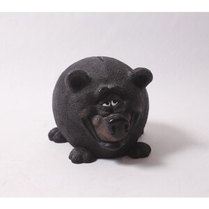 May include: A black bear-shaped money box with a smiling face. The ceramic bank has a round body, small ears, and a brown snout. The bear is sitting on all fours, with its paws visible.