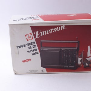 May include: An Emerson PM3911 portable radio in its original box. The box is white with a red and white design and the Emerson logo. The radio is black with a handle and antenna. The box text reads "TV/WB/FM/AM AC/DC Portable Radio".