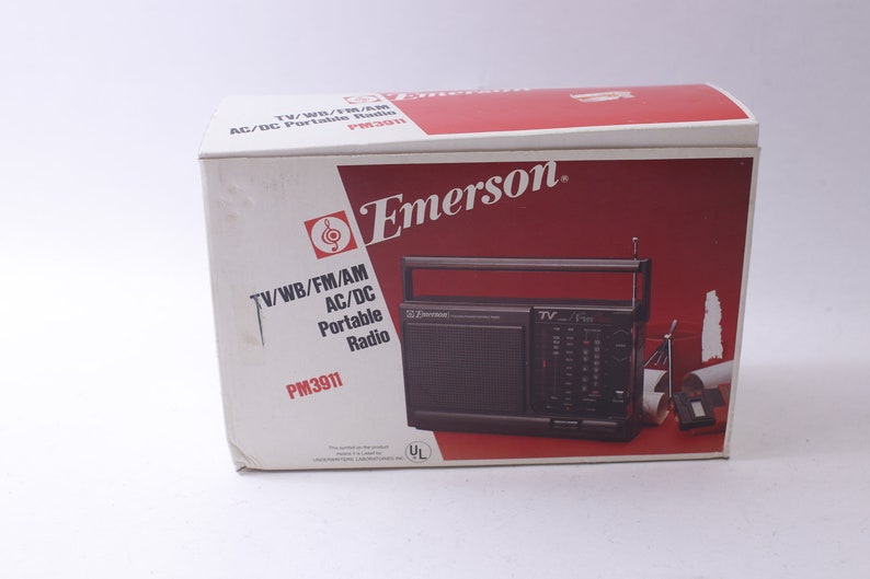 May include: An Emerson PM3911 portable radio in its original box. The box is white with a red and white design and the Emerson logo. The radio is black with a handle and antenna. The box text reads "TV/WB/FM/AM AC/DC Portable Radio".