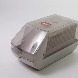 May include: A gray and clear plastic Staples-branded stapler with a stack of staples visible inside. The stapler has a clear plastic cover and a red Staples logo on top. The base is a light gray color.