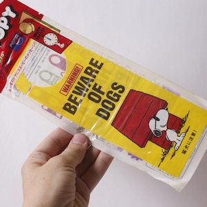 May include: A Snoopy themed door hanger in original plastic packaging. The yellow sign features a red doghouse, a Snoopy illustration, and the text WARNING! BEWARE OF DOGS. The top header includes the Snoopy logo, Pepsi branding, and a clock graphic.