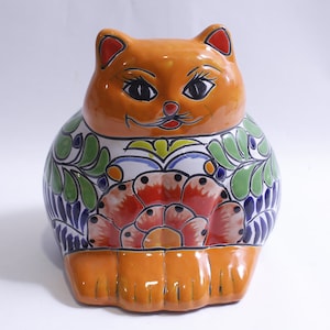 May include: A ceramic orange cat figurine with colorful floral designs. The cat is sitting with its paws crossed and has a friendly expression.