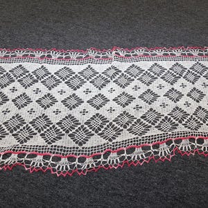 May include: A rectangular white crochet doily featuring a repeating diamond pattern with floral motifs inside each shape. The edges are finished with a delicate scalloped border accented by a thin, vibrant pink thread trim throughout the perimeter.