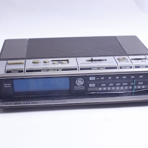May include: A black and silver General Electric AM/FM digital clock radio with a blue fluorescent display. The radio has a sleep, display set, radio, wake, volume, and band buttons. The radio has a dial with FM and AM frequencies.