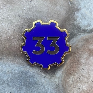 Op de afbeelding: Een gouden metalen pin met een blauwe achtergrond en het nummer 33 in wit.