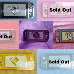 Puede incluir: Colección de pines de esmalte con forma de consola de juegos, cada uno con un diseño único en la pantalla. Los pines presentan varios colores, incluyendo negro, rosa, morado, amarillo y azul. Algunos pines tienen el texto "Sold Out".
