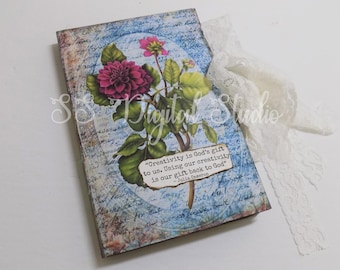 Op de afbeelding: Een vintage-stijl dagboek met een bloemenontwerp en een citaat over creativiteit. Het citaat luidt: "Creativiteit is Gods geschenk aan ons. Ons gebruik van onze creativiteit is ons geschenk terug aan God." - Julia Cameron