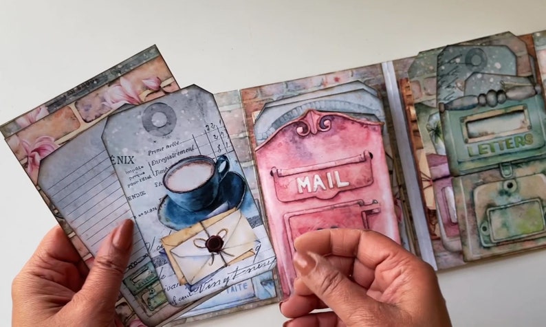 May include: A scrapbook with a vintage mail theme. The pages feature images of mailboxes, letters, and a cup of coffee. The scrapbook is decorated with paper scraps, tags, and embellishments.