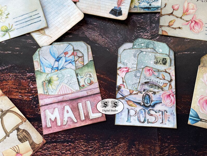 May include: Two decorative mail and post envelopes with a vintage aesthetic. The envelopes are decorated with floral patterns, including magnolia blossoms, and have a layered, dimensional look. The envelopes are labeled "MAIL" and "POST" in a distressed font.