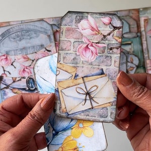 May include: A set of vintage-style paper tags with floral and brick designs. The tags feature images of pink magnolia flowers, envelopes tied with twine, and a brick wall. The text "Lettres" is visible on one of the tags.