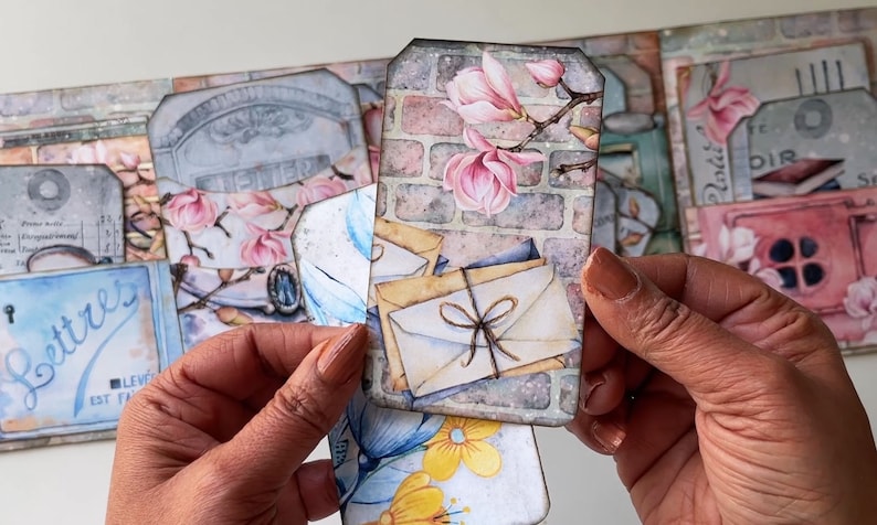 May include: A set of vintage-style paper tags with floral and brick designs. The tags feature images of pink magnolia flowers, envelopes tied with twine, and a brick wall. The text "Lettres" is visible on one of the tags.