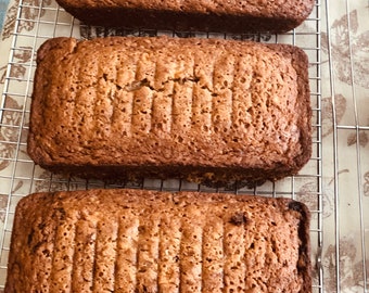 May include: Three loaves of freshly baked bread cooling on a wire rack. The bread is golden brown and has a slightly crispy crust.