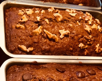 May include: Three loaves of banana bread in baking pans. The loaves are topped with chocolate chips, walnuts, and cranberries.