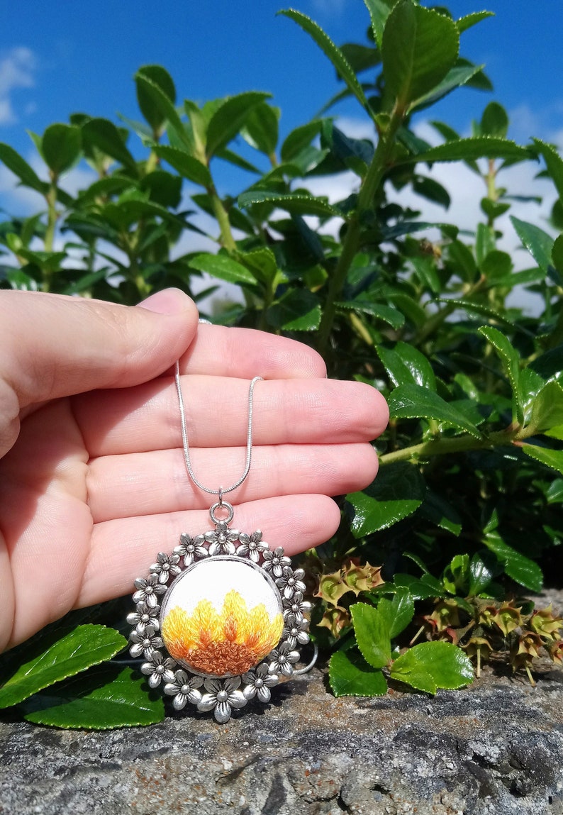 Sunflower embroidered onto a silver floral pendant