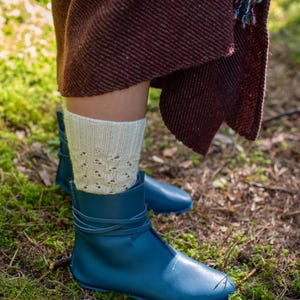 May include: A pair of blue leather boots with laces, worn with white knitted socks. The boots are on a bed of green moss.