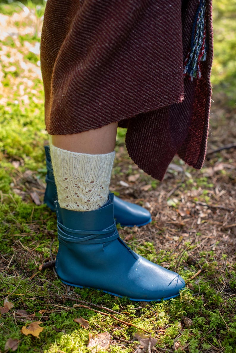 May include: A pair of blue leather boots with laces, worn with white knitted socks. The boots are on a bed of green moss.