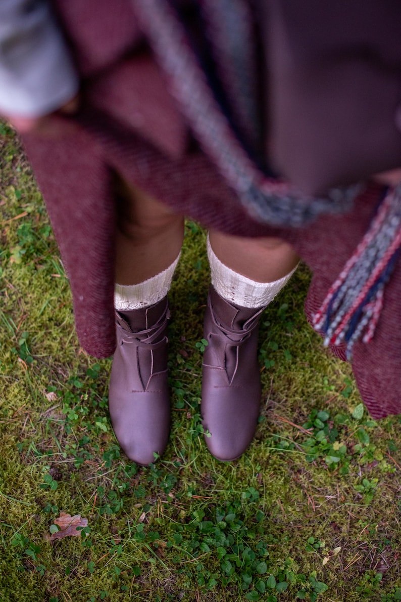 May include: A pair of brown leather lace-up boots with white socks. The boots are worn by a person standing on a bed of green moss.