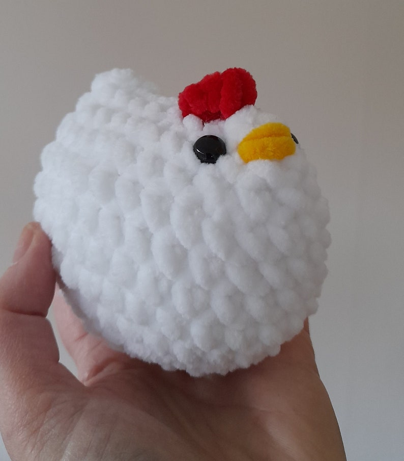 Puede incluir: Un juguete de pollo de peluche blanco hecho a mano, con una cresta roja, ojos negros y un pico amarillo. El pollo suave y redondo se sostiene en una mano, mostrando su textura esponjosa y su dise&ntilde;o caprichoso. Este adorable juguete es perfecto para ni&ntilde;os.