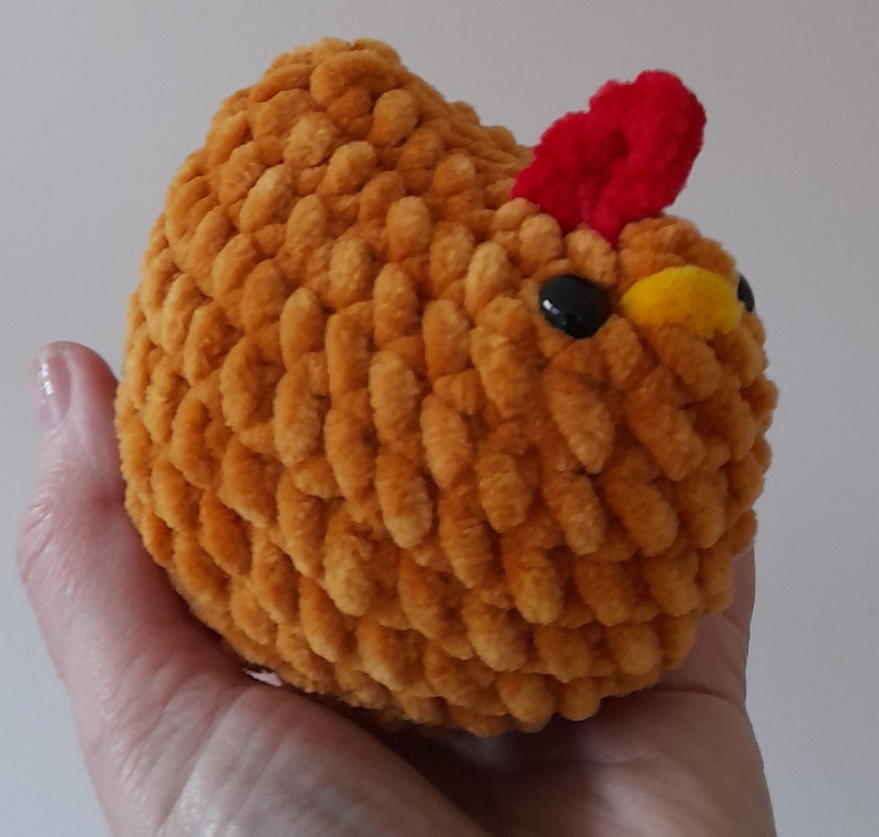 Puede incluir: Un juguete de pollo de peluche hecho a mano en un c&aacute;lido tono naranja. El pollo presenta una cresta roja, ojos negros y un pico amarillo. El material suave y texturizado le da al juguete una apariencia tierna. Este art&iacute;culo artesanal es probablemente un juguete para ni&ntilde;os o un objeto decorativo.