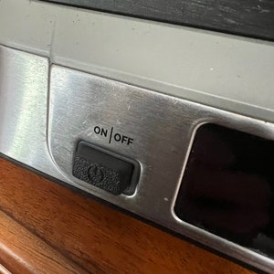 May include: Close-up of a silver appliance with a black on/off switch. The switch has a power symbol on it.