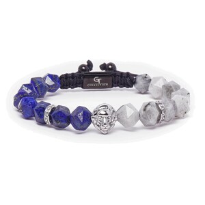 May include: A blue and grey beaded bracelet with a silver lion head charm. The bracelet has a black cord with the text "GT COLLECTION" on it.