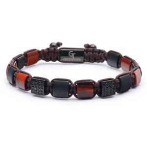 Peut inclure: Un bracelet tressé marron avec des perles carrées noires et rouges. Certaines des perles noires sont serties de diamants noirs. Le bracelet porte une étiquette métallique sur laquelle est inscrit "GT COLLECTION".
